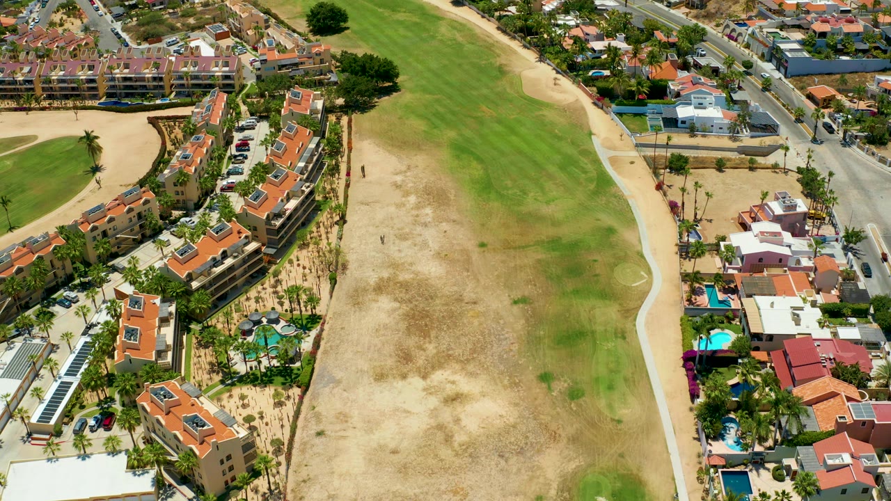 Elevated view across a field with houses, pools, and a road.