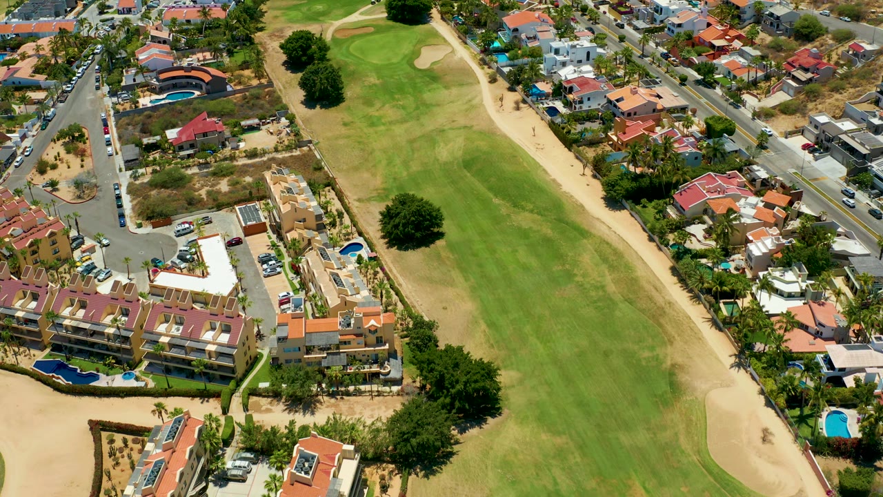 Overhead drone view of homes, streets, pools, and a green golf course.