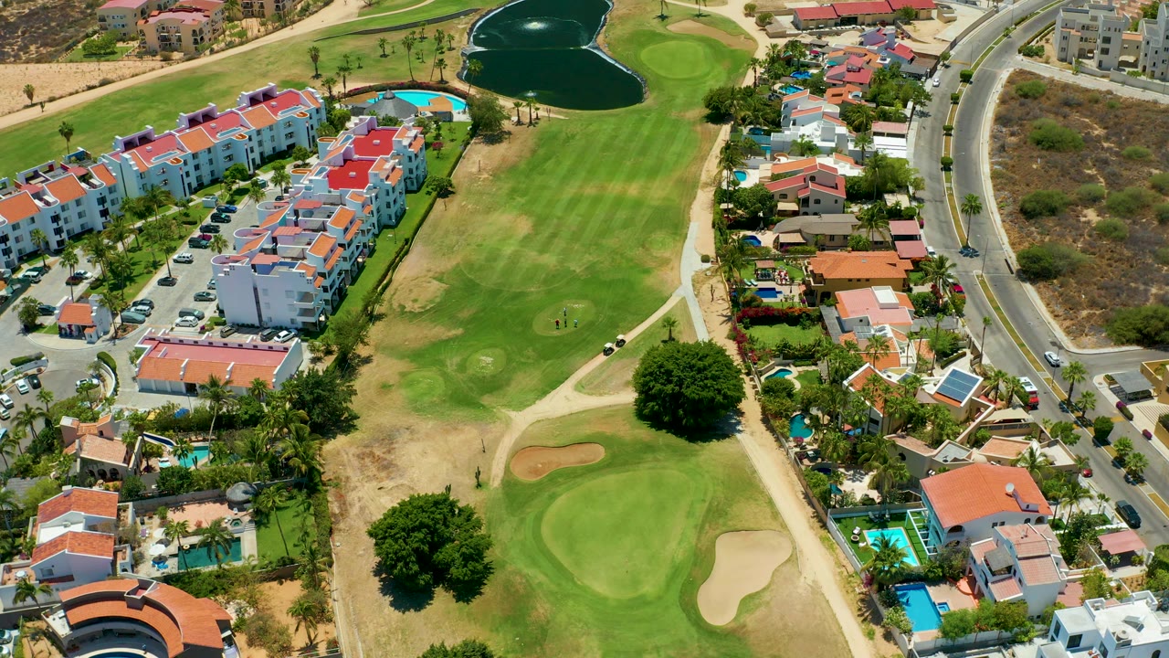 High aerial view of golf greens, sand traps, houses, pools, and road traffic.