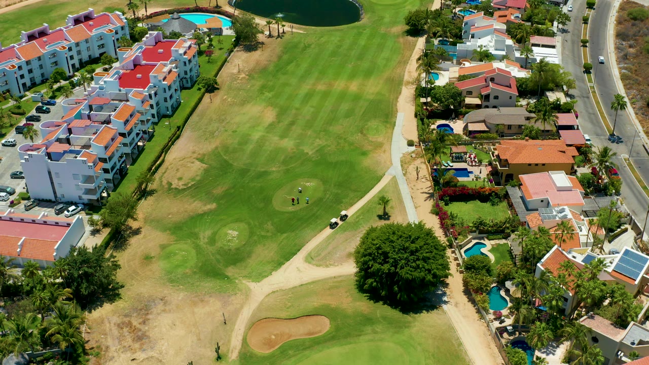 Golf fairway with nearby villas, road, pools, and small golfers.