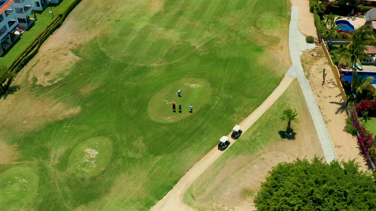 Aerial golf course frame with people on the green and carts near the path.