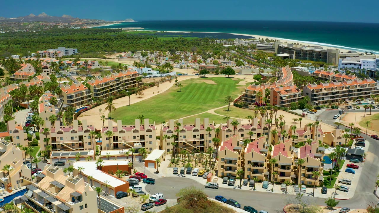 Drone view over red-roof buildings, a golf course, and coastline.