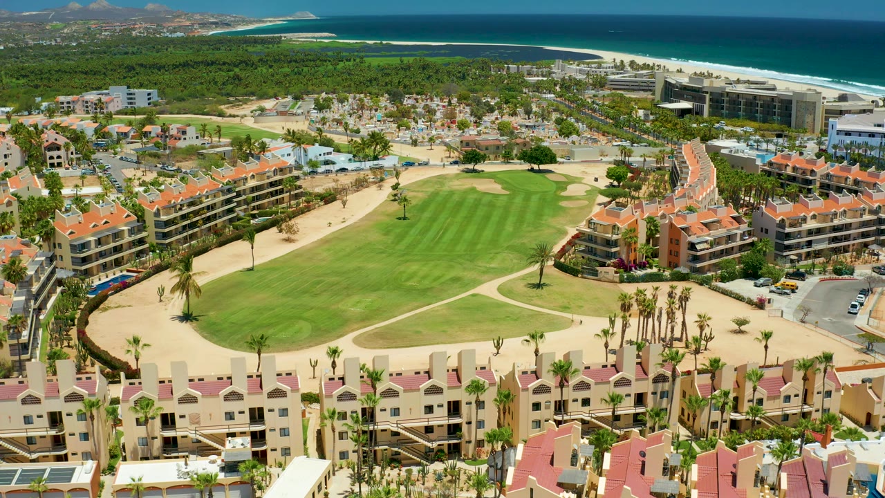 Golf course and red-roofed buildings near a sandy beach and blue water.