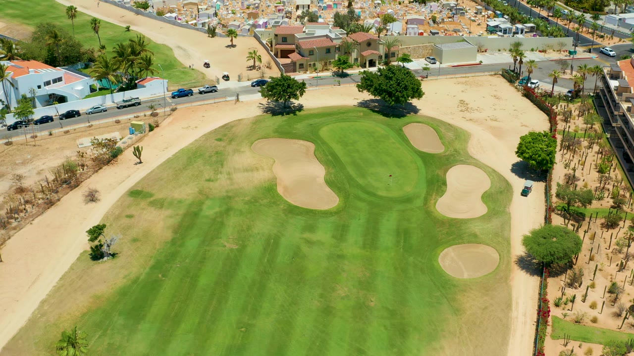 Drone view of golf fairway, sand bunkers, road traffic, and desert lots.