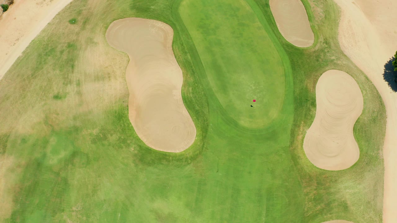 Top-down view of a San Jose del Cabo golf green bordered by tan sand traps, with a tiny ball near the putting surface and no visible people.