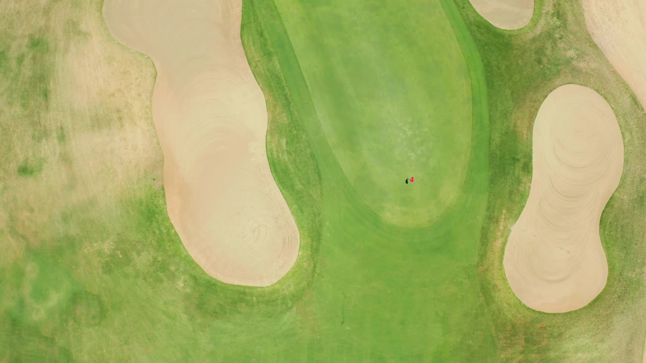 A high overhead frame shows the San Jose del Cabo green, tan sand traps, patchy rough, and a tiny ball or marker near the putting area, with no visible people.
