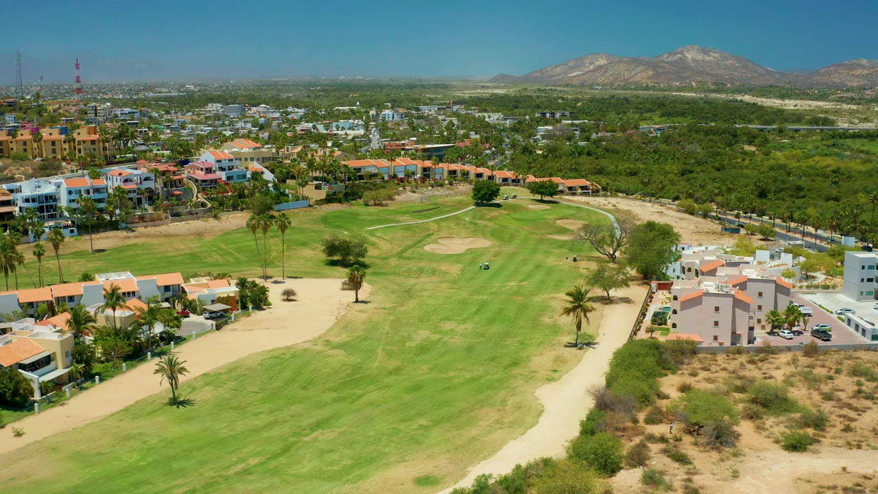 Aerial view across a golf course toward homes and mountain hills.