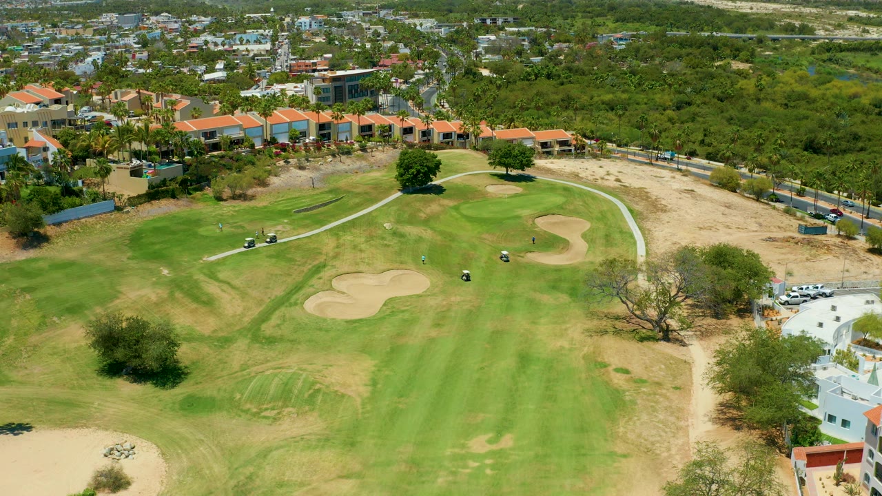 Elevated golf course view with carts on the grass and sand traps near a residential edge.