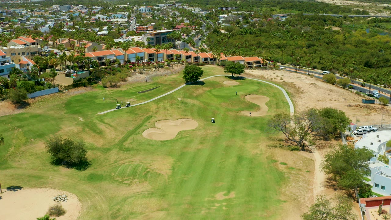 Elevated golf course view with carts near a path and sand traps on the green.