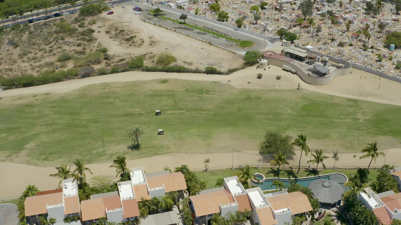 Aerial golf fairway with cart and sandy access road near homes.