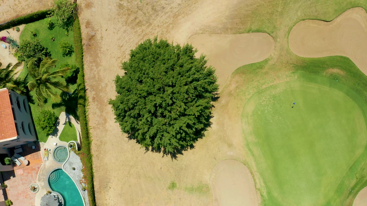 Top-down golf course corner with house, pool, tree, sand traps, and dry grass.