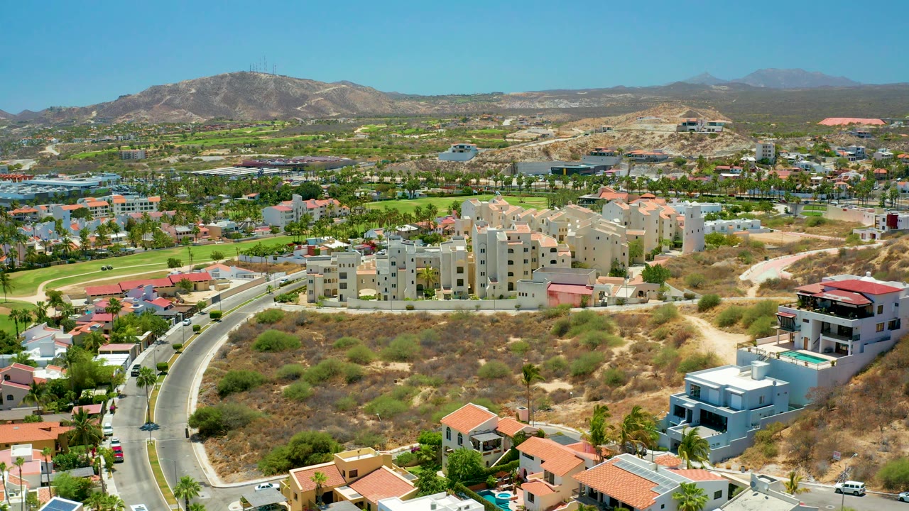 San Jose del Cabo aerial view with the winding road along the lower left, modern homes at the lower right, apartment blocks in the midground, mountains on the horizon, and no visible people.