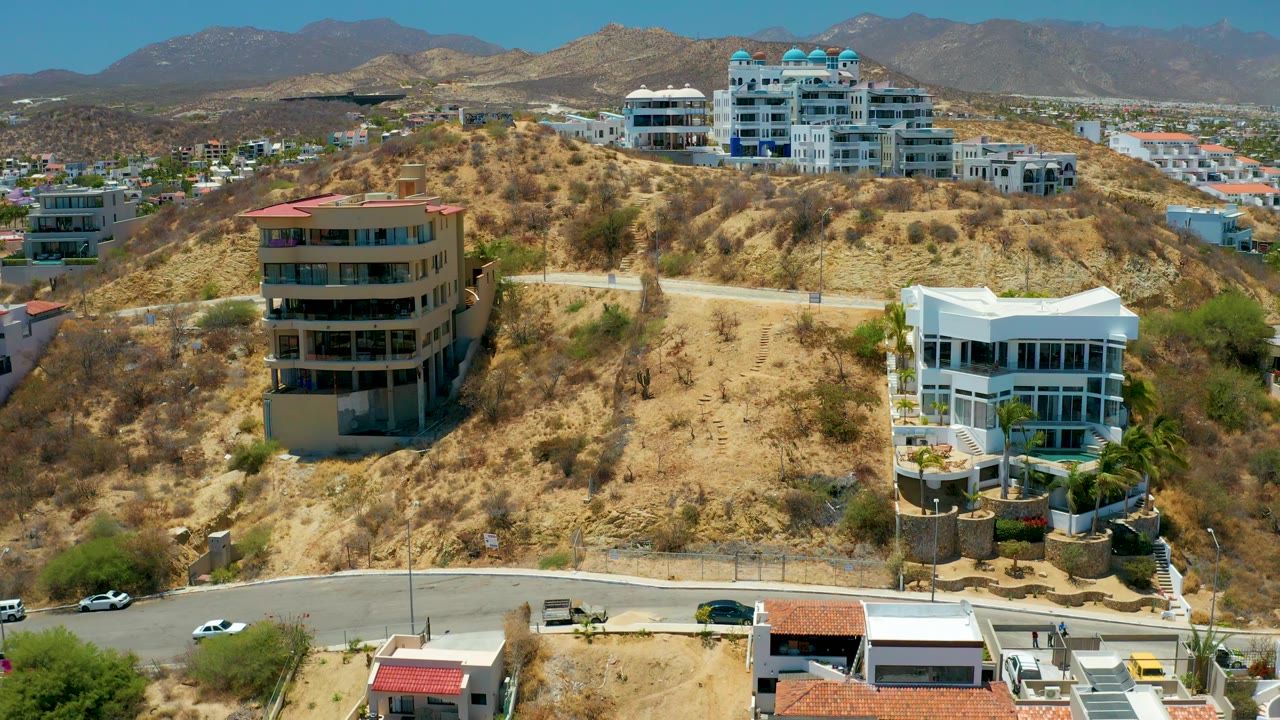 Aerial hillside neighborhood with cars on the road and mountains behind.