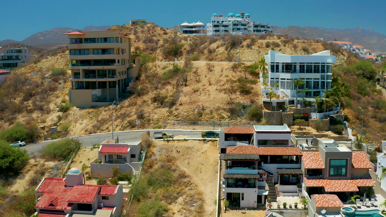 Residential hillside with a beige apartment-style building, white modern house, and road.