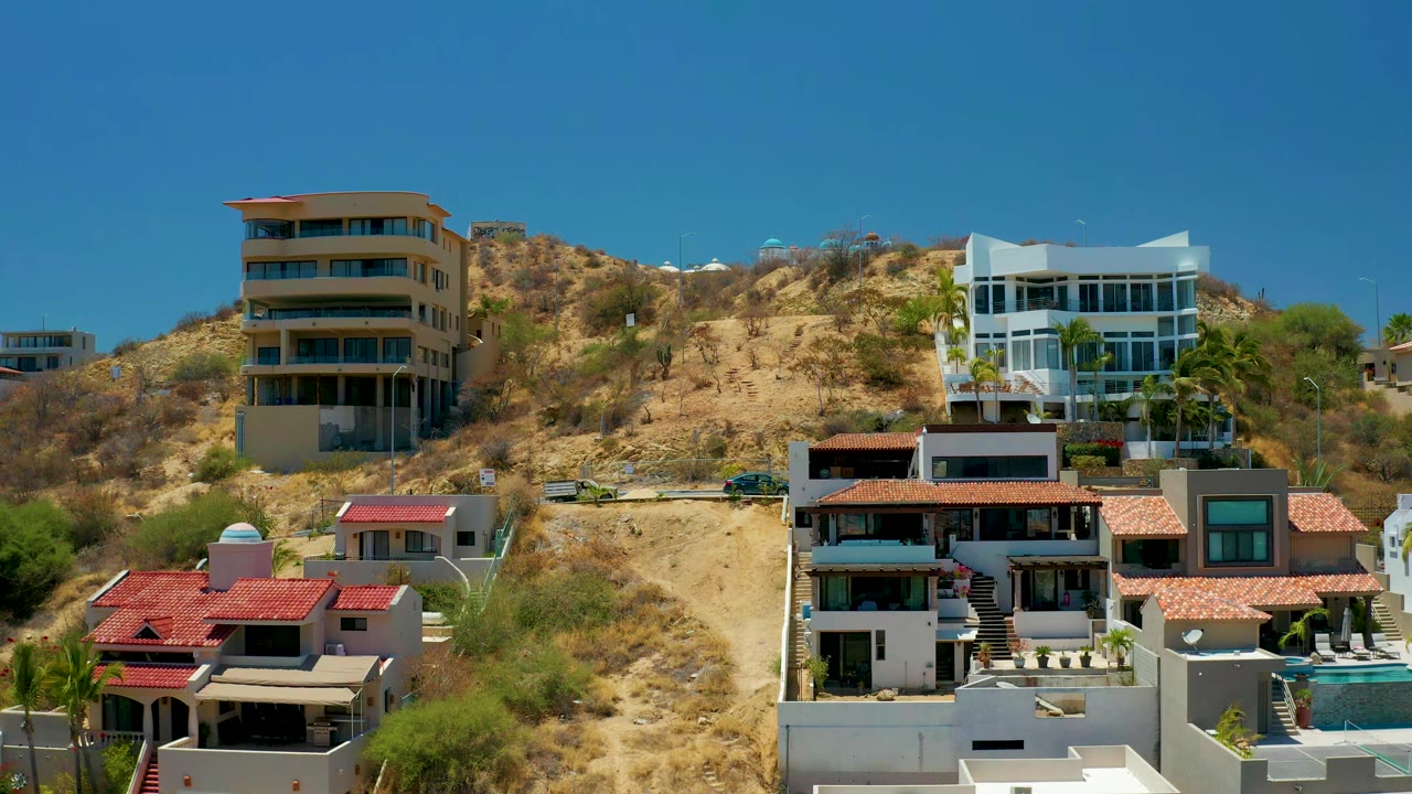 San Jose Del Cabo hillside residences fill the frame, with larger apartment-style buildings above smaller white homes and no visible people.