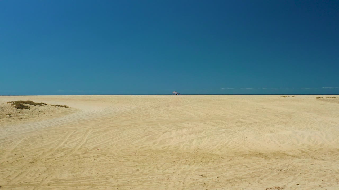 Flat beach landscape with pale sand, ocean horizon, and blue sky.