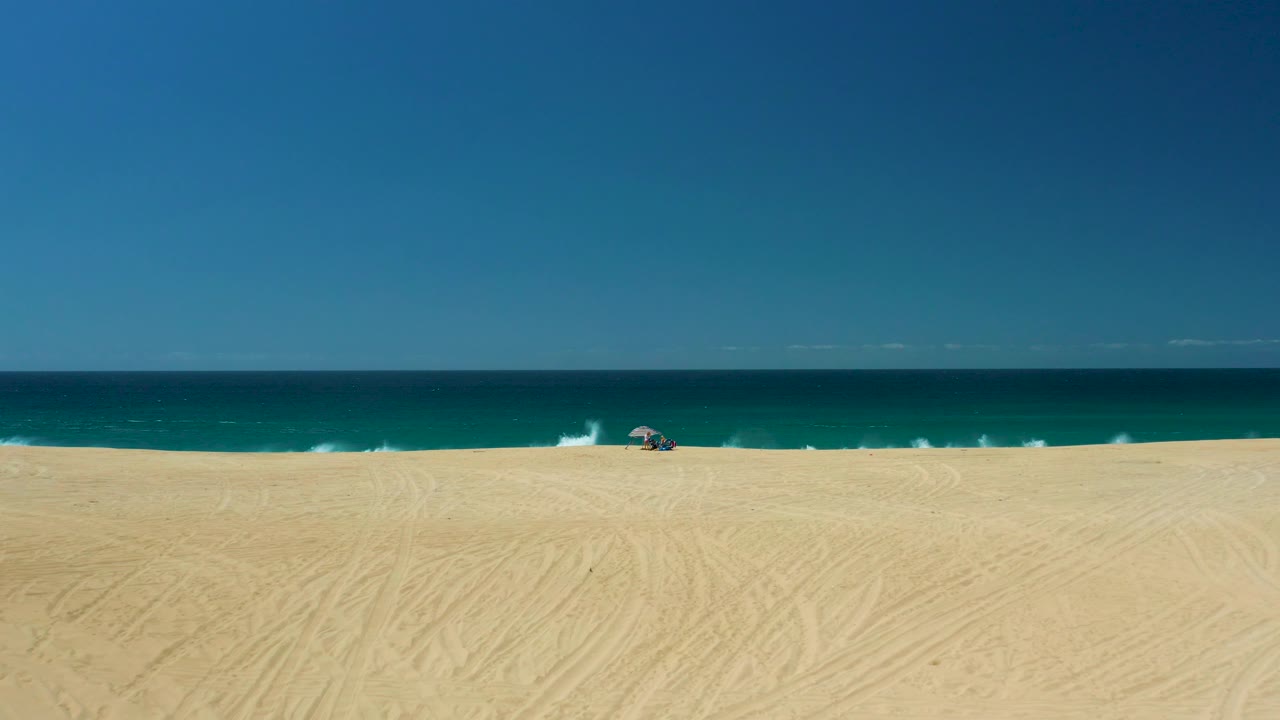 Wide beach view with waves breaking farther left and a small umbrella near the surf.