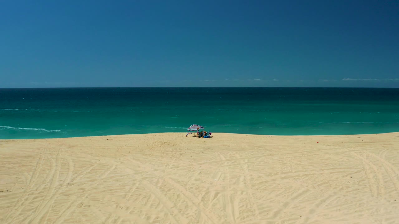 The third frame shows La Laguna Beach Los Cabos with the umbrella shifted toward the right side of the beach, visible people beneath it, and smooth turquoise water behind.