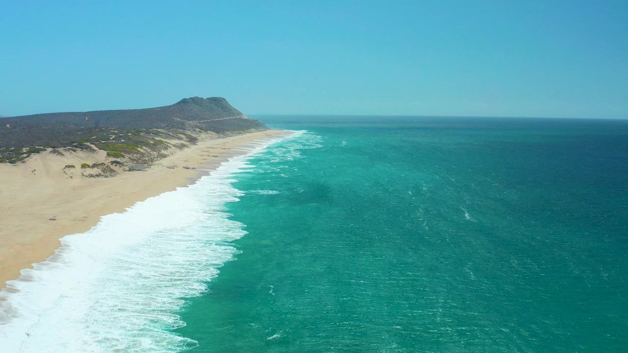 Aerial view of turquoise ocean waves breaking along a sandy beach.