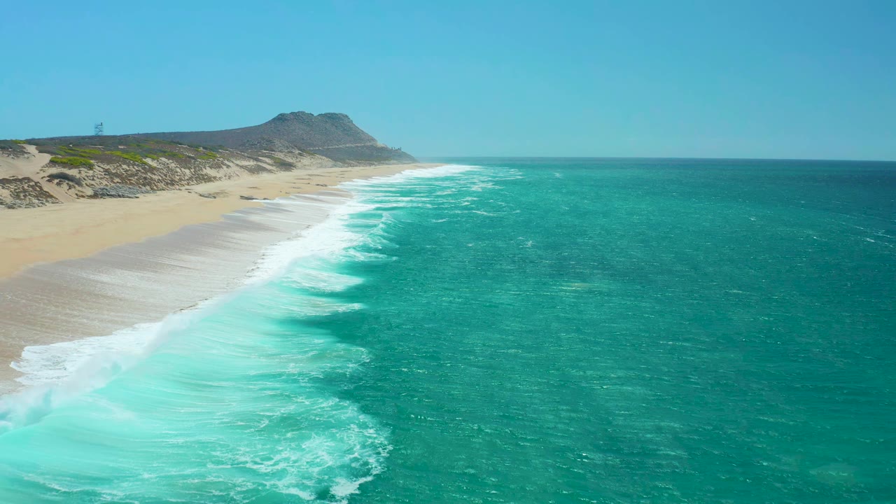 At 0:01, a wider band of white foam curls into the beach at La Laguna Beach Los Cabos while the open turquoise water fills most of the frame and no visible people appear.