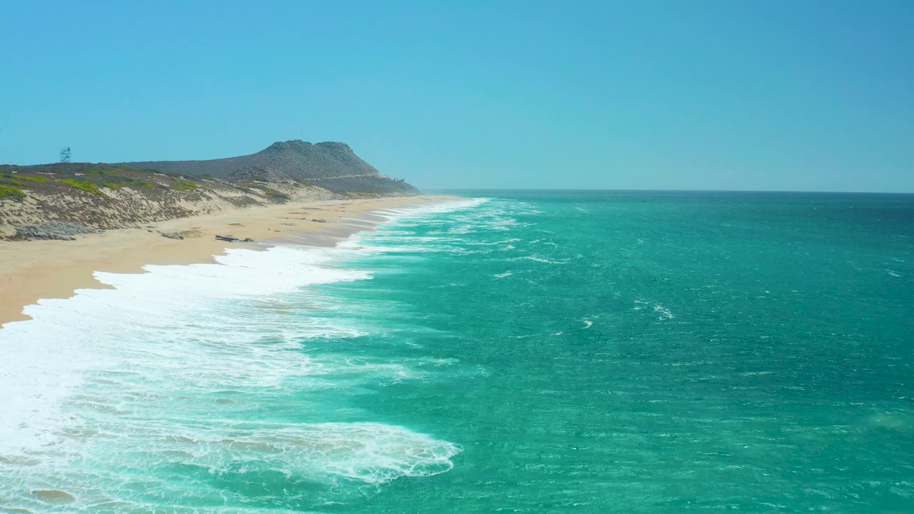 Wide beach and ocean view with foam bands rolling toward shore.