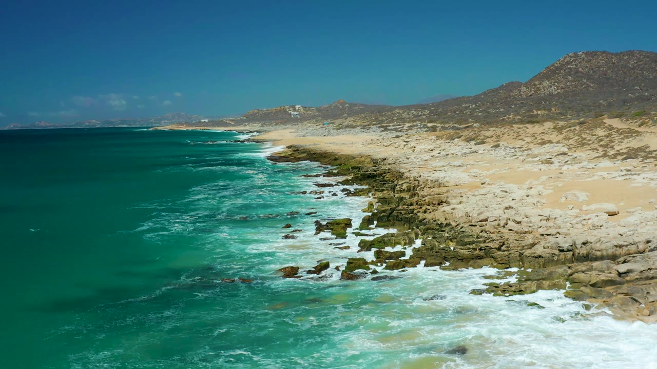 Surf washing over rocks along a pale sandy coastline
