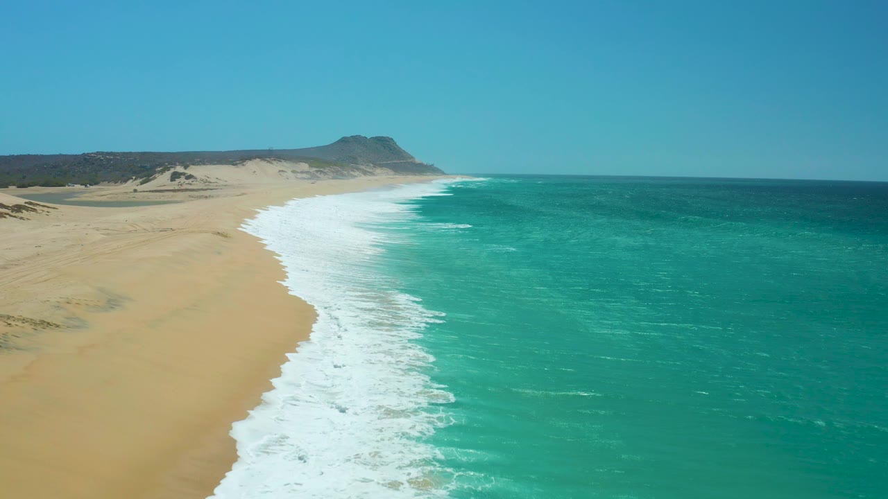 High coastal view of surf tracing a sandy beach under clear sky.