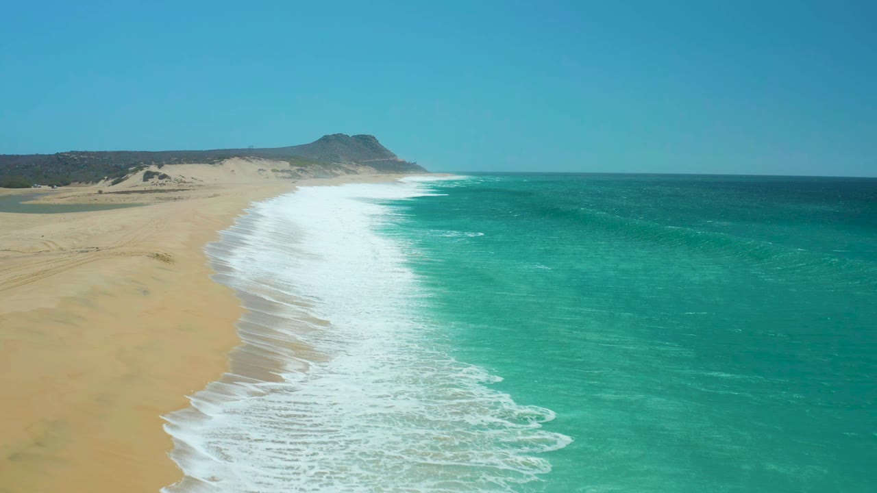 Aerial view of La Laguna Beach showing whitewater spread farther across the wet sand, with deep blue water offshore and no visible people.