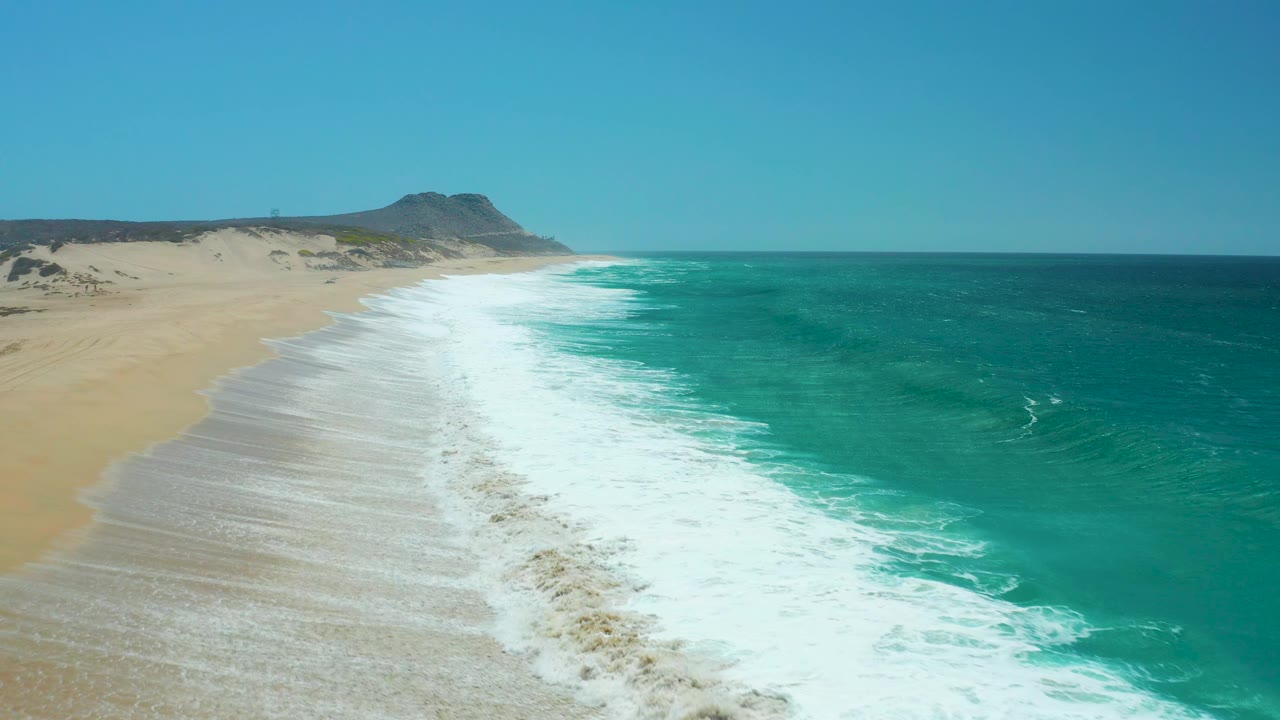 La Laguna Beach appears from a slightly later moment with the surf band shifted down the shoreline, pale sand on the left, turquoise water on the right, and no visible people.