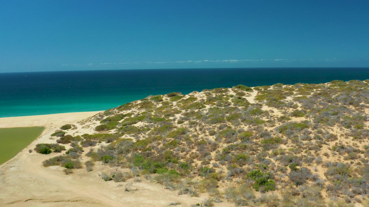 Aerial view of sandy coastal dunes beside turquoise ocean.