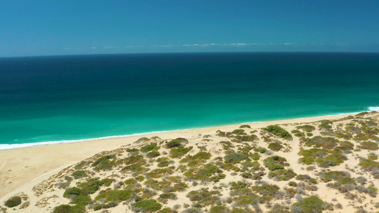 Dunes and beach below a wide turquoise ocean
