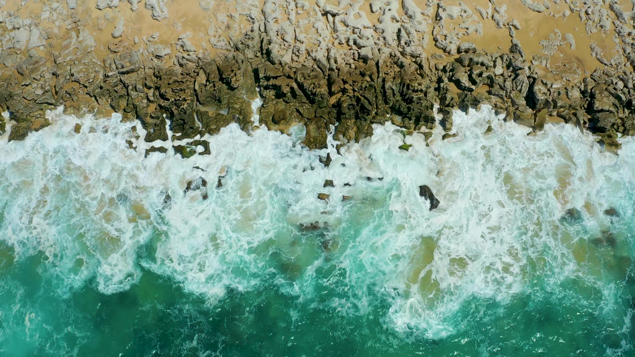 A broad white breaker covers the center of the rocky shore.