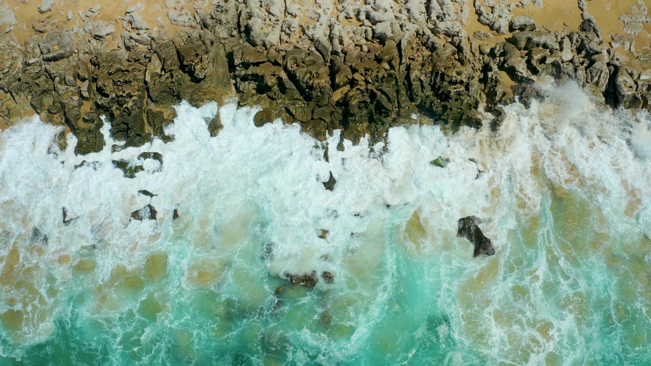Turquoise surf breaking over dark coastal rocks