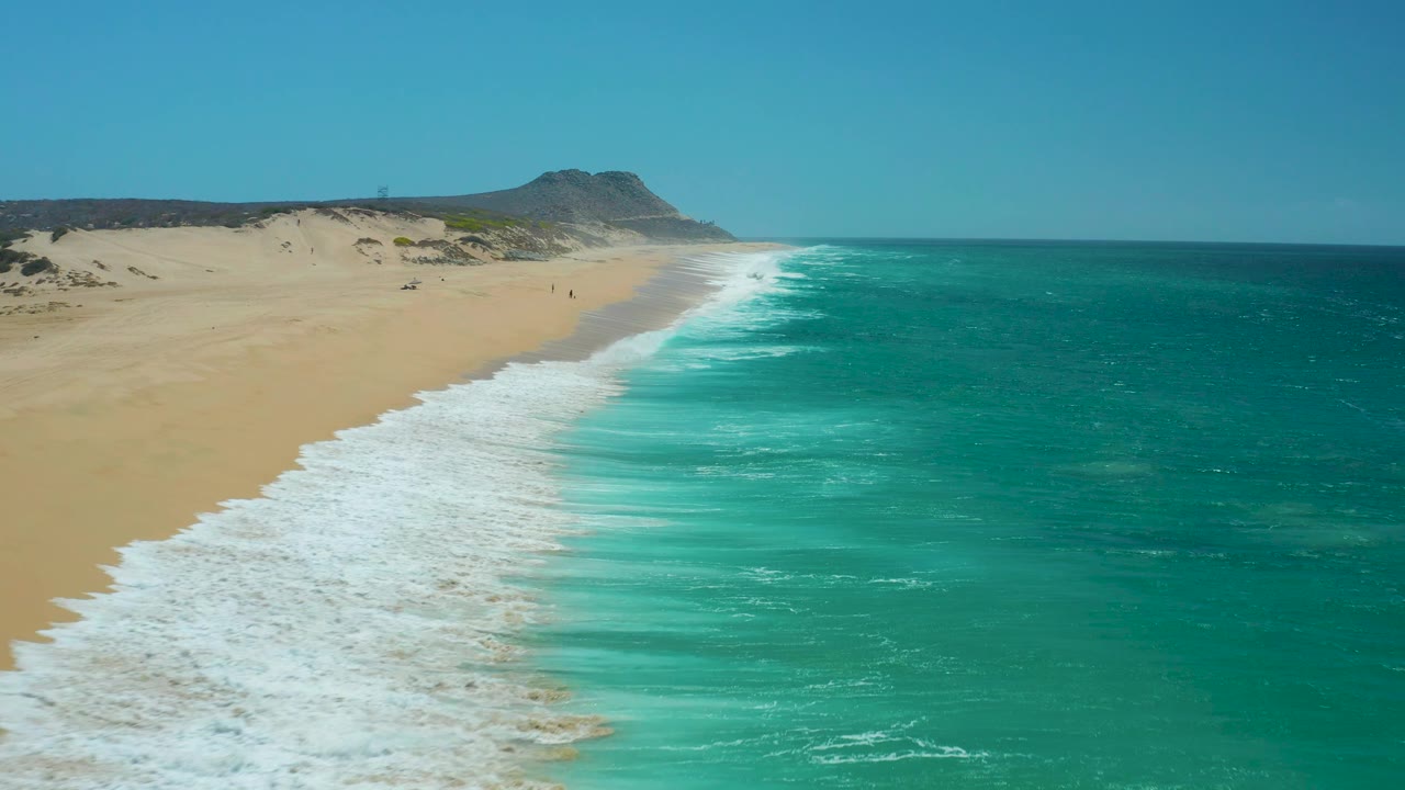 Foam washes up a long diagonal stretch of sandy beach.