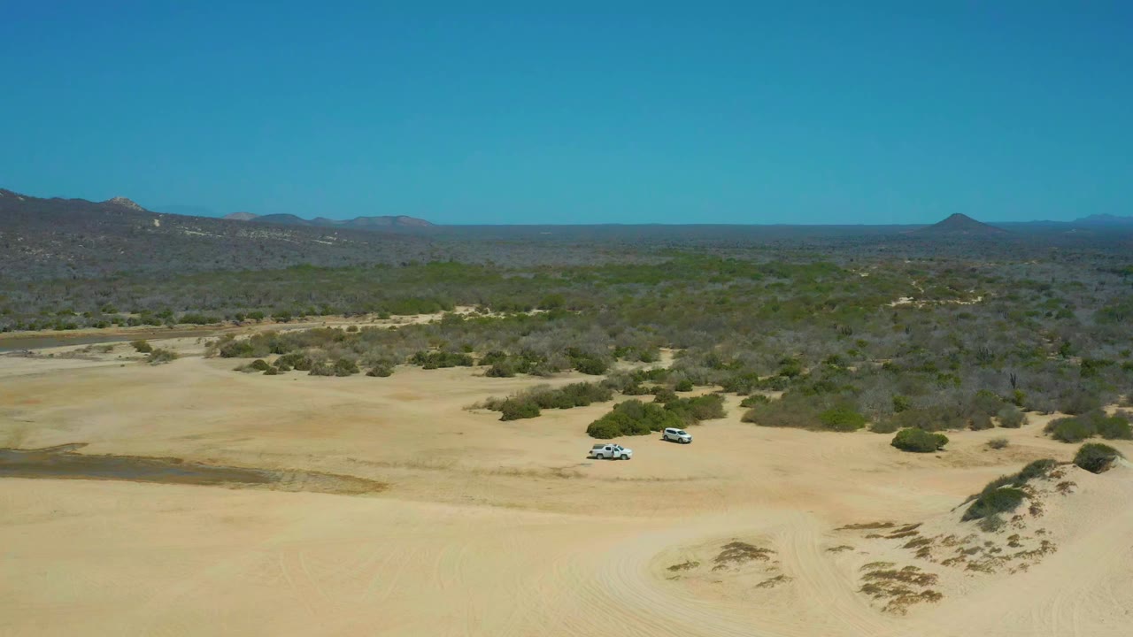 Two SUVs on sandy dunes with shrubs and distant mountains.