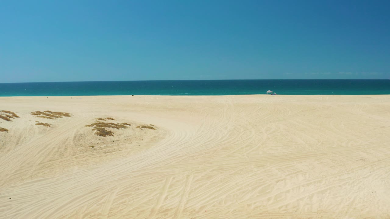Beach dunes and ocean under clear blue sky.