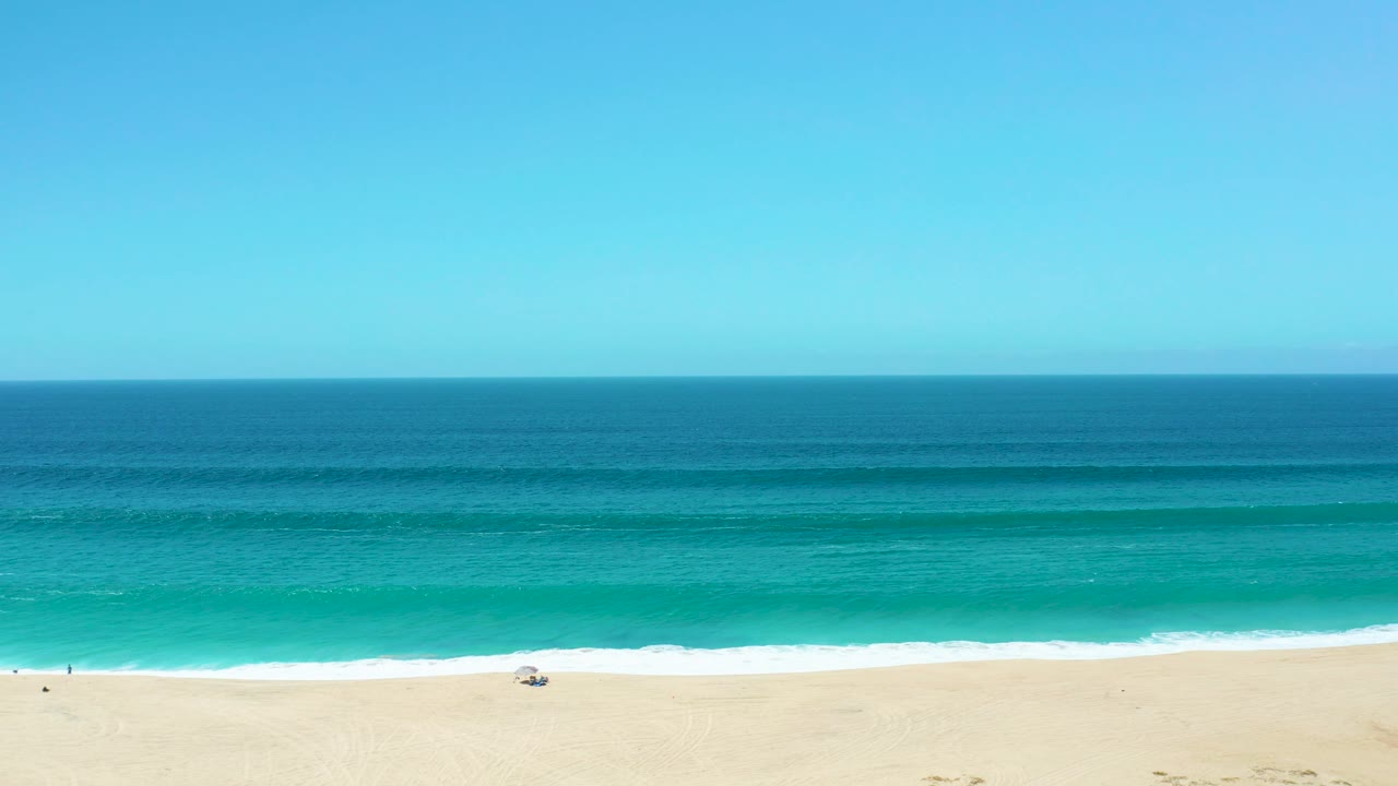 Sandy shoreline with rolling surf and small figures at the far left.