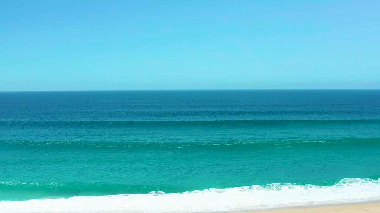 La Laguna Beach Los Cabos ocean view with the wave crest stretching across the midground, white surf at the bottom edge, clear sky above, and no visible people.