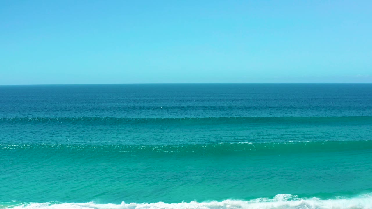 La Laguna Beach Los Cabos shoreline view with more sky visible above layered turquoise water, a low breaking wave near the lower frame, and no visible people.