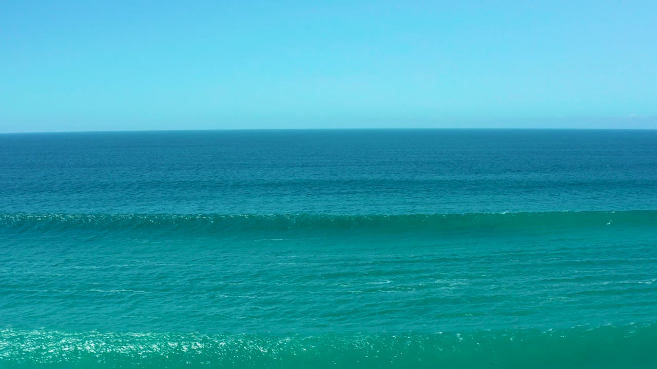Turquoise ocean water at La Laguna Beach Los Cabos with a low band of swell beneath a clear blue sky and no visible people.