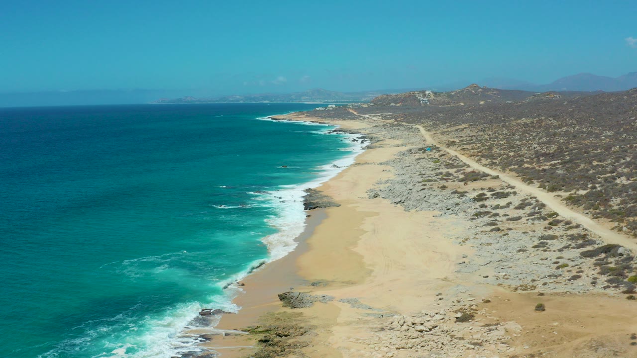 Aerial view of turquoise ocean, sandy beach, and coastal dirt road.