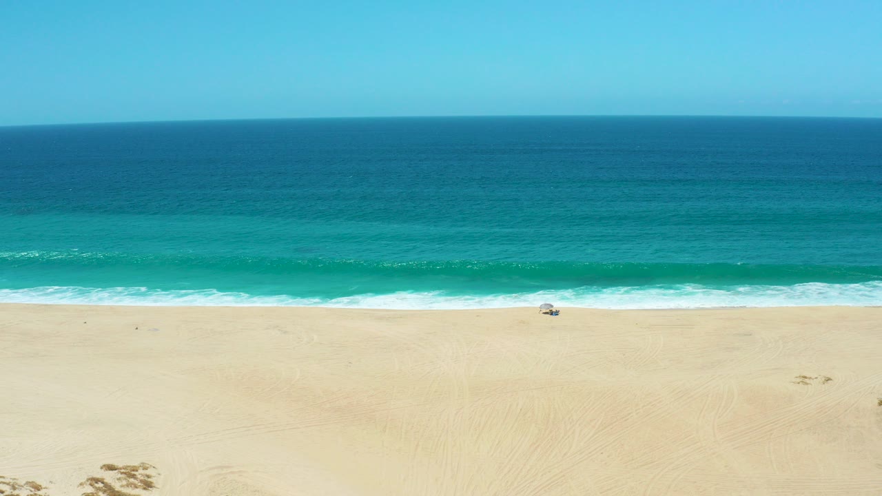 La Laguna Beach Los Cabos, Mexico, seen from an elevated angle with deep blue water, a turquoise nearshore band, pale sand, and no visible people.