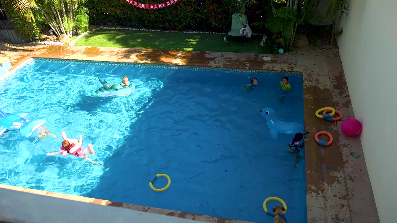 Children float and swim in a sunlit backyard pool.