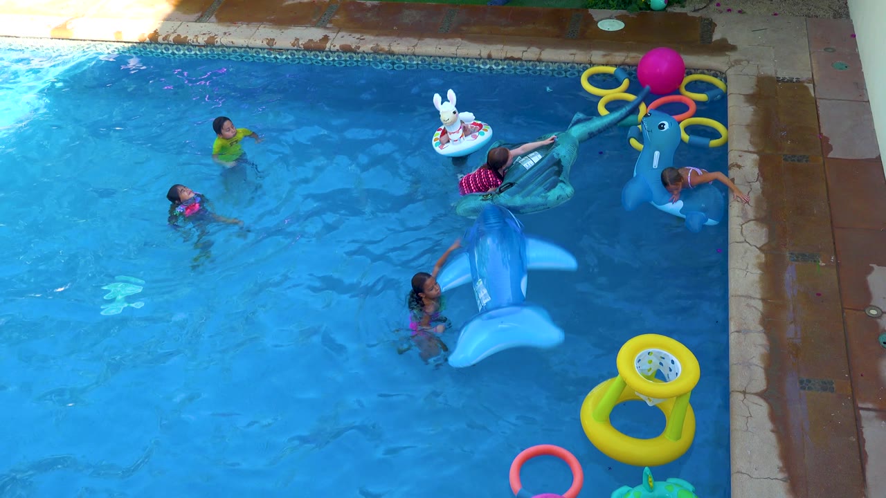 A child rides near the dark inflatable float at the upper right while another child holds the large blue dolphin float in the San Jose Del Cabo backyard pool.
