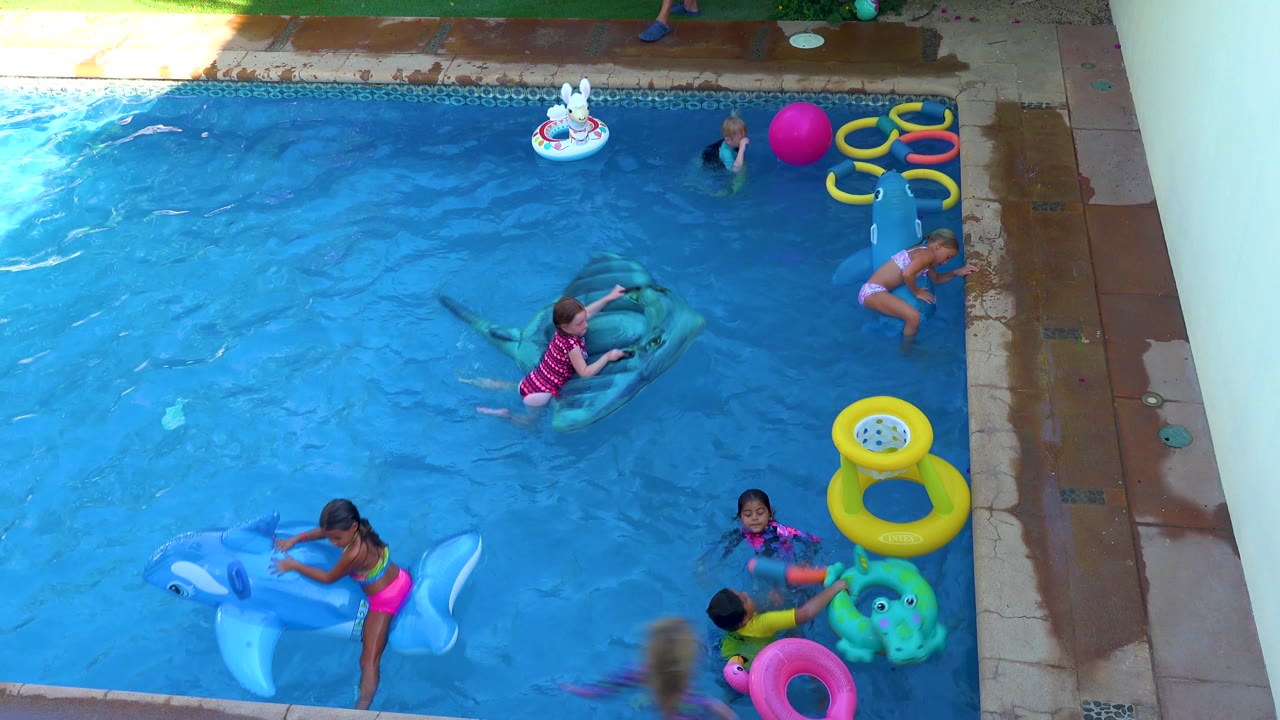 In San Jose Del Cabo, children play among pool toys while one child reclines on a green shark float, another stands at a blue float, and a pink ball floats near the right side.
