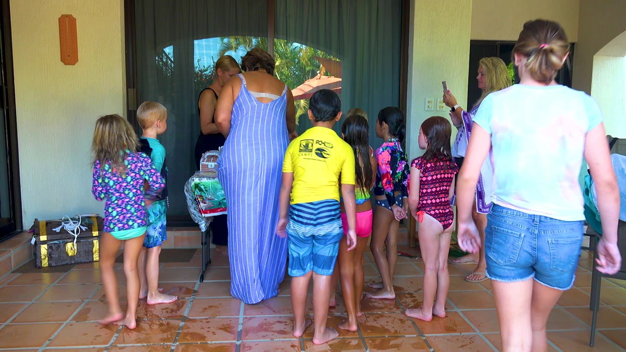 Group of children in swimwear facing adults on a wet patio.