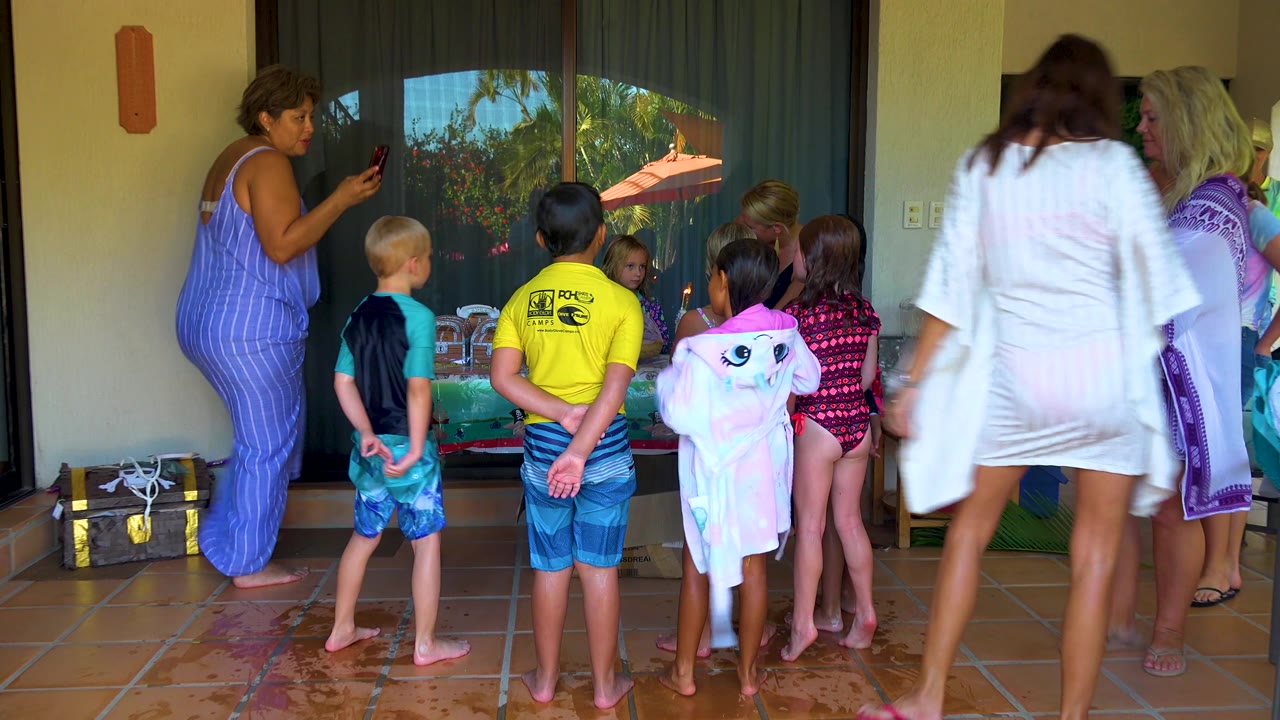 In San Jose Del Cabo, the group shifts closer to the table, with a child in a pink towel near center and adults in blue and white coverups at the edges.