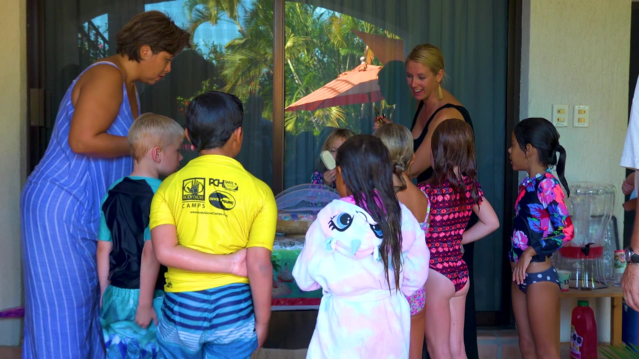 Adults talk with children gathered near drinks on a patio table.