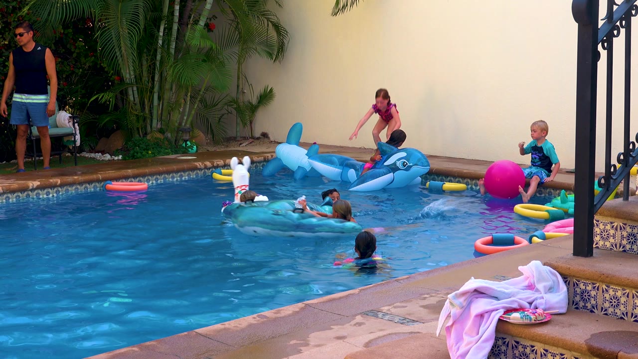 Children gather around pool floats while an adult stands beside the pool.