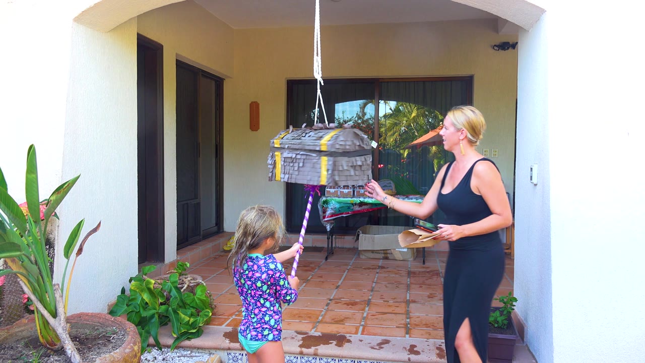 Woman gestures near the piñata while the girl holds the stick.